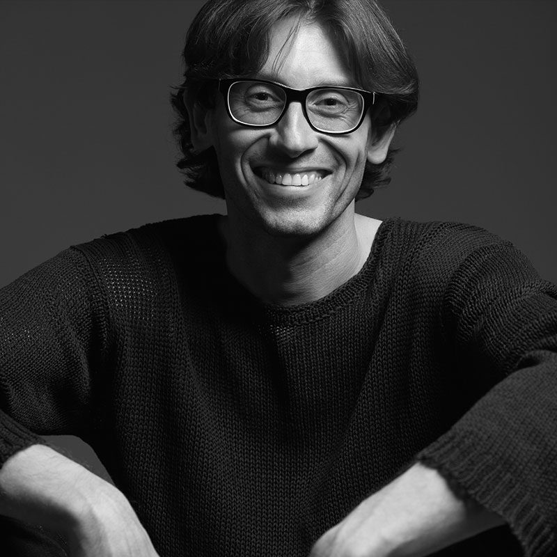 A man with glasses sitting in front of a black background.