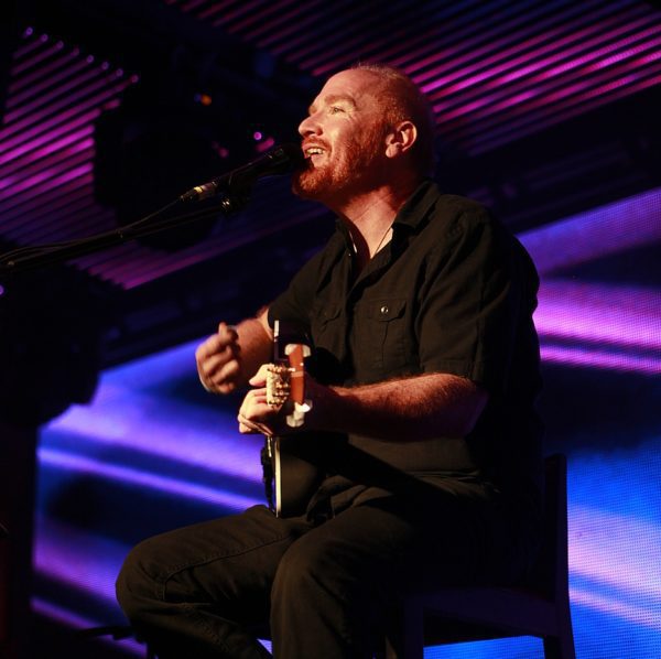 Singer performing on stage with guitar.