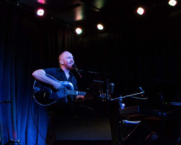 A man playing an acoustic guitar on stage.