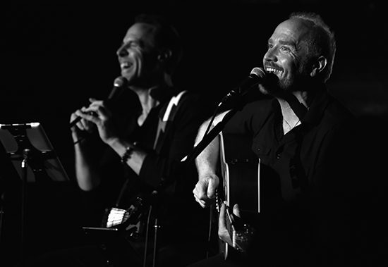 Two musicians performing with guitars and microphones.